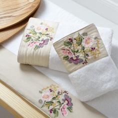 two white towels with flowers on them are sitting on a wooden table next to a plate