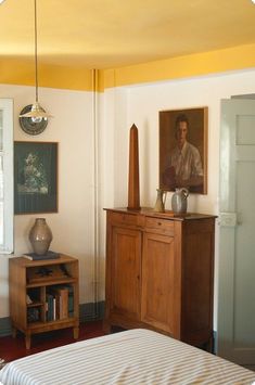 a bed sitting next to a wooden dresser in a room with paintings on the wall