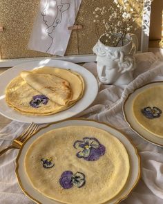 three pancakes on white plates with purple pansies painted on them and gold trim