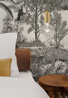 a bed with white sheets and pillows in front of a jungle wallpaper