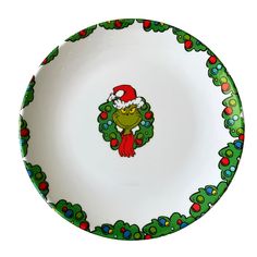 a white plate with a green and red christmas wreath on the rim, decorated with an image of a frog wearing a santa hat