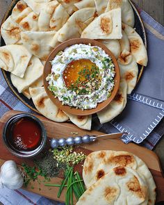 pita breads with dip and vegetables on a platter next to a bowl of sauce