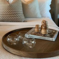 a wooden tray with three wine glasses and a book on it, sitting on a bed