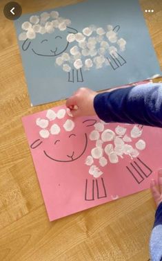 a child's hand is drawing on paper with flowers and sheeps in the background