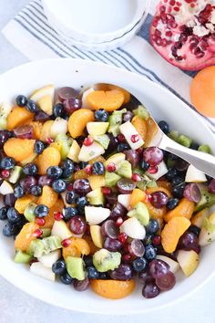 a white bowl filled with fruit next to an orange and pomegranate