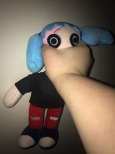 a hand holding a stuffed animal with big eyes and blue hair on it's head