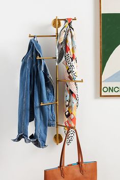 a coat rack with clothes hanging on it next to a purse