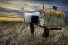 an old mailbox sitting in the middle of a field with tall grass on either side