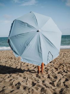 a person is holding an umbrella on the sand at the beach while standing under it