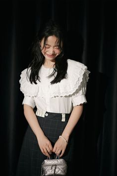 a woman in a white shirt and black skirt holding a silver purse with her hands