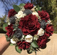 a bridal bouquet with red, white and black flowers is held in someone's hand