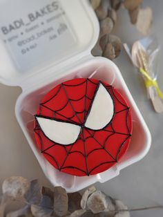 a spiderman cake in a plastic container on the table next to rocks and spoons