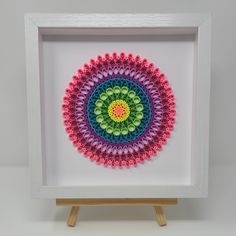 a white frame with a multicolored circular design in it on top of a wooden easel