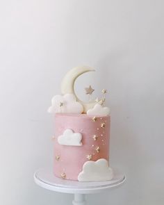 a pink and white cake with stars, clouds and a moon on top is sitting on a table