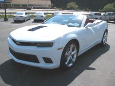 a white chevrolet camaro convertible parked in a parking lot with other cars behind it