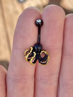 an octopus belly ring is being held in someone's hand with gold and black accents