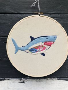 a hand embroidered shark is hanging on a wall with wood planks in the background