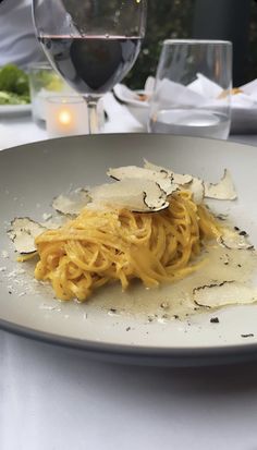 a white plate topped with pasta and sauce next to a glass of wine on a table