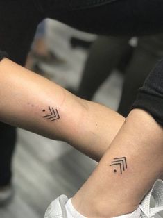 two people with matching tattoos on their arms, one is holding the other's arm