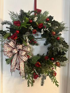 a wreath hanging on the front door with red and white flowers, greenery and holly