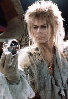 a man with long blonde hair holding a crystal ball in his right hand and looking at the camera