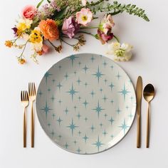 a white plate with blue stars on it next to two gold forks and some flowers