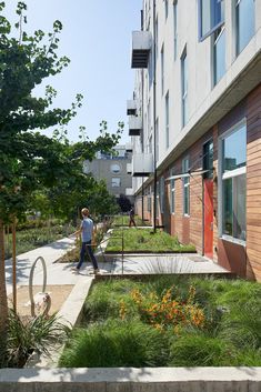 a man walking down a sidewalk next to a tall building with lots of green plants