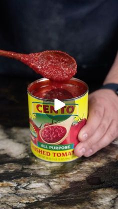 a person holding a spoon full of canned tomato soup with the lid open and it is being held up