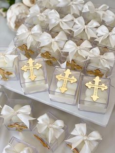 several small boxes filled with white and gold cross cookies on top of a table covered in bows