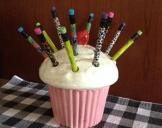 a cupcake with lots of pens sticking out of it's side on a checkered table cloth