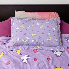 a bed with two pillows and one pillow on top of the covers is covered by purple sheets