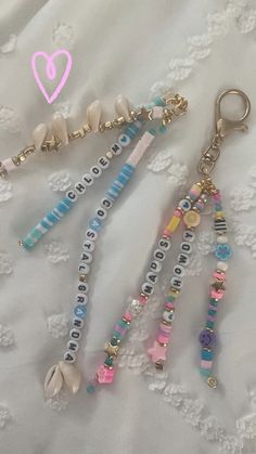 three different key chains with beads and charms on top of a white lace covered surface