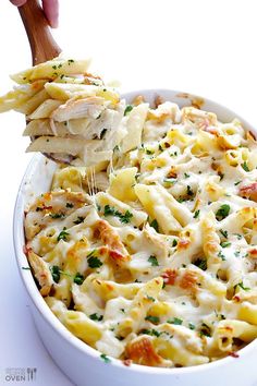 a wooden spoon scooping some pasta from a casserole dish with chicken and cheese