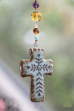 a cross hanging from the side of a window with beads attached to it's sides