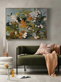 a living room with a green couch and white flowers on the wall above it is an orange throw pillow