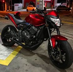 a red and black motorcycle parked in a parking lot next to a gas station at night