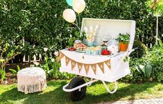 an outdoor party with balloons, cake and desserts on a cart in the grass