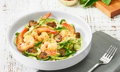 a white bowl filled with shrimp and veggies next to a knife and fork