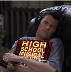 a man sleeping with headphones on his ears while holding a high school musical book