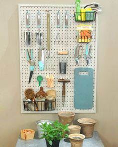 a peg board with pots and gardening tools hanging on it's wall next to a potted plant