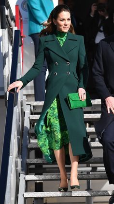 a woman in a green dress and coat walking down stairs with her hand on her hip