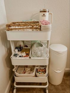 a white cart filled with lots of items next to a trash can and toilet paper