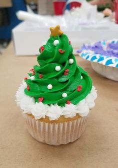 a cupcake decorated with green frosting and a christmas tree on top is sitting on a table