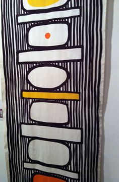 an art piece hanging on the wall in front of a white wall with black and orange designs