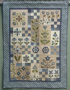 a quilted wall hanging on the side of a green building with blue and white flowers