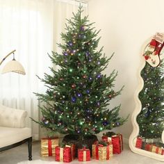 a decorated christmas tree in a living room next to a mirror with presents under it