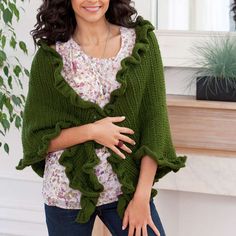 a woman standing in front of a fireplace wearing a green knitted sweater with ruffles