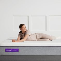 a woman laying on top of a purple mattress in the middle of a white room