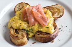 a white plate topped with slices of bread covered in scrambled eggs and salmon on toast