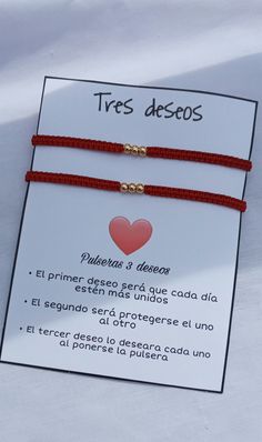 two red string bracelets with gold heart charms on white carded paper and spanish text